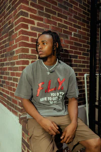 a man sitting on a brick wall wearing a t - shirt that says fly